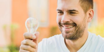 Homem segurando lâmpada ao descobrir Como economizar energia em casa.